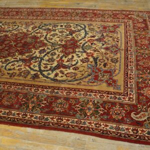 Ornate red and tan patterned rug with scrolling floral and vine motifs displayed on distressed yellow wood flooring.