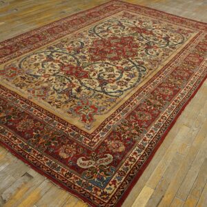 Beige and red traditional area rug with large floral medallion rests on worn wooden flooring.