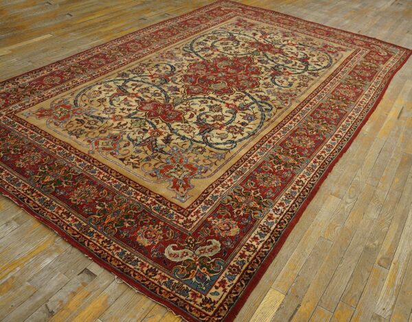 Beige and red traditional area rug with large floral medallion rests on worn wooden flooring.