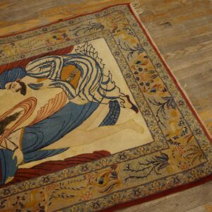Beige rug with a central blue and red figural design and complex yellow floral borders on hardwood.