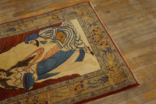 Beige rug with a central blue and red figural design and complex yellow floral borders on hardwood.