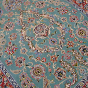 Teal patterned rug with ornate floral designs in cream, red, and blue resting on a wooden floor.