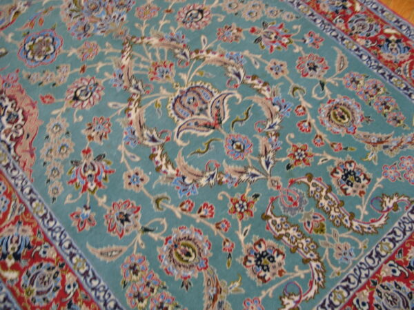 Teal patterned rug with ornate floral designs in cream, red, and blue resting on a wooden floor.