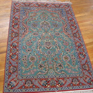 Ornate aqua rug with floral medallion and detailed red borders rests on light wood plank flooring.