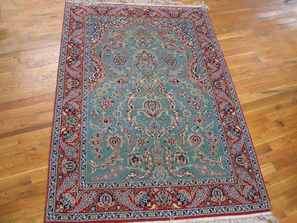 Ornate aqua rug with floral medallion and detailed red borders rests on light wood plank flooring.