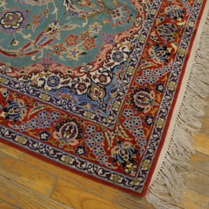 Teal and red patterned rug corner with fringe rests on light brown distressed wood flooring.