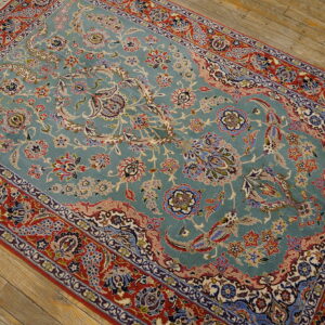 Teal and red floral patterned rug with visible fringe laid upon distressed wooden plank flooring.