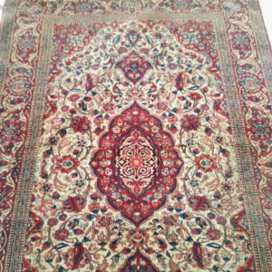 Detailed traditional rug featuring a large red and blue medallion on a cream field with ornate floral borders.
