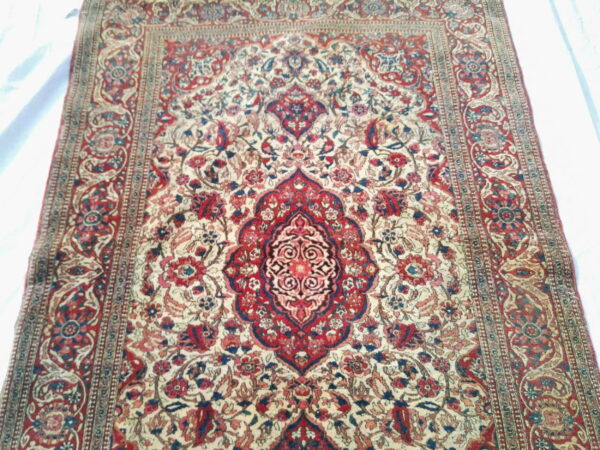Detailed traditional rug featuring a large red and blue medallion on a cream field with ornate floral borders.