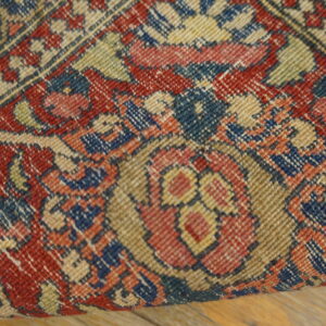 Detailed view of a low-pile rug featuring red, blue, and beige traditional floral patterns on wood planks.