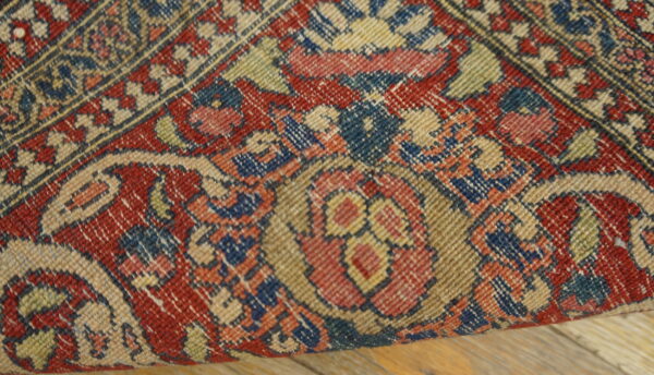 Detailed view of a low-pile rug featuring red, blue, and beige traditional floral patterns on wood planks.