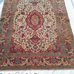 Red and cream traditional rug featuring a central medallion and intricate floral motifs displayed on white sheeting.