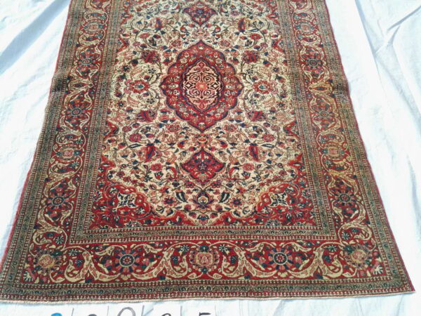 Red and cream traditional rug featuring a central medallion and intricate floral motifs displayed on white sheeting.