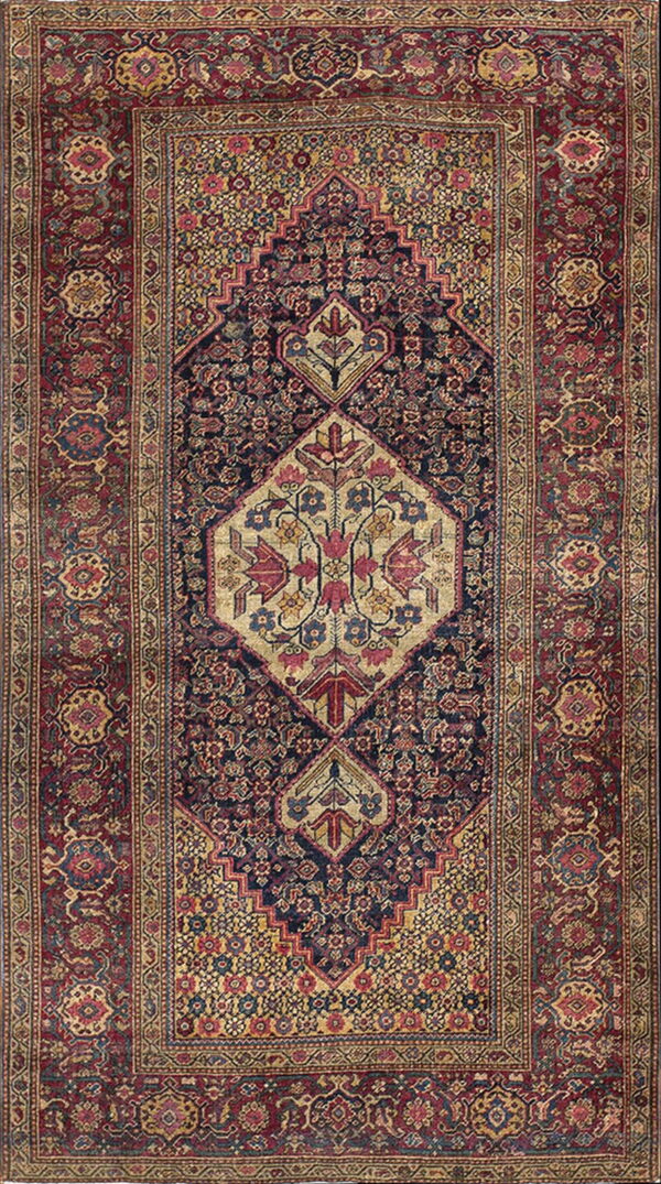 Intricate traditional rug featuring a dark blue central field, a tan medallion, and wide red floral borders.