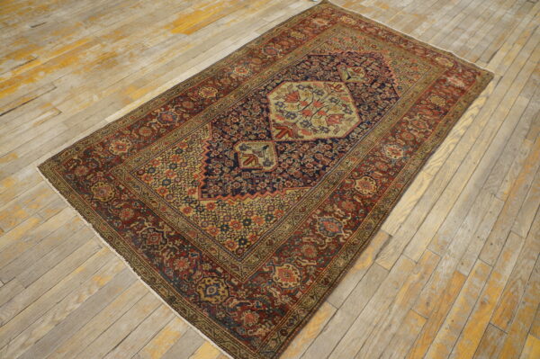 Muted red and blue low-pile rug with a complex hexagonal floral medallion on distressed plank flooring.
