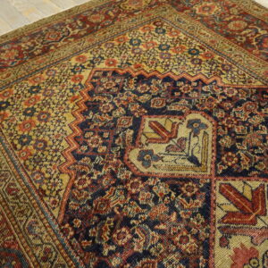 Intricate, low-pile rug in navy, gold, and red floral-geometric patterns resting on distressed wood planks.
