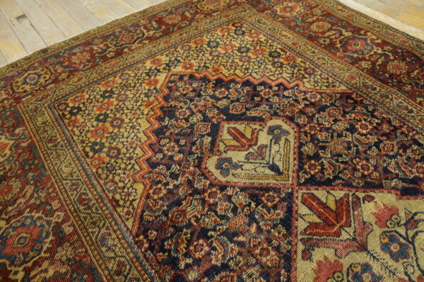 Intricate, low-pile rug in navy, gold, and red floral-geometric patterns resting on distressed wood planks.