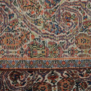 Detailed view of a tightly woven rug border separating cream, blue, and red traditional floral motifs.