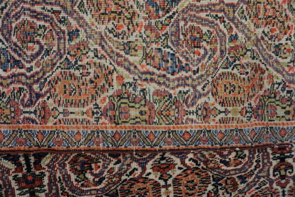 Detailed view of a tightly woven rug border separating cream, blue, and red traditional floral motifs.