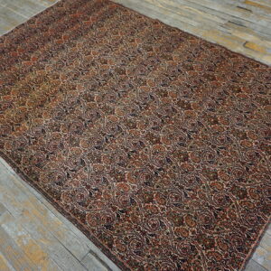A low-pile area rug with dense repeating patterns in rust, navy, and tan rests on distressed gray wood floors.
