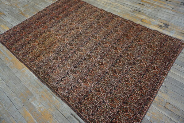 A low-pile area rug with dense repeating patterns in rust, navy, and tan rests on distressed gray wood floors.