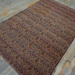 Ornate red, tan, and navy rug featuring continuous paisley motifs on rustic gray wood floors.