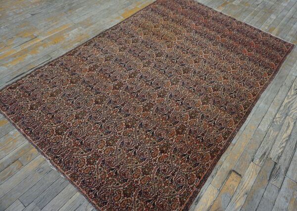 Ornate red, tan, and navy rug featuring continuous paisley motifs on rustic gray wood floors.