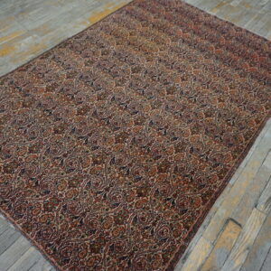 Detailed red, navy, and cream repeating paisley rug covering distressed gray wood floors.