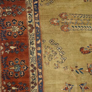 Detail of an olive-green rug field next to a rust and blue floral border on distressed yellow flooring.