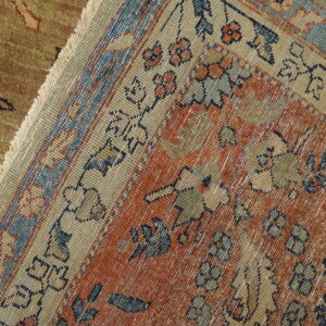 Detailed view of a rust orange, blue, and beige patterned rug with fringes laid over a textured brown rug.