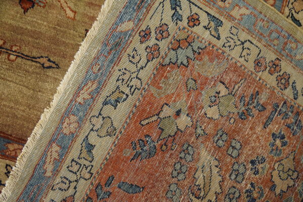Detailed view of a rust orange, blue, and beige patterned rug with fringes laid over a textured brown rug.