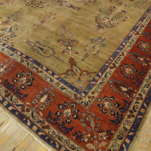 Muted olive green rug with blue and rust floral patterns and a wide terracotta border on plank wood flooring.