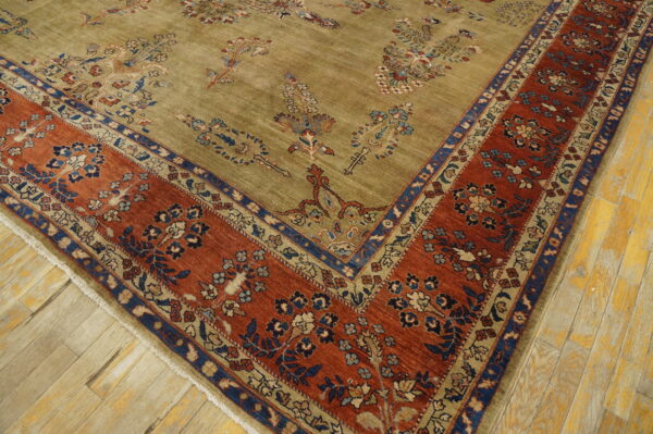 Muted olive green rug with blue and rust floral patterns and a wide terracotta border on plank wood flooring.