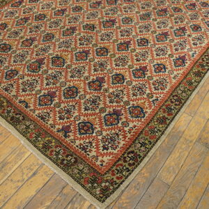 Beige rug with repeating orange, blue, and green geometric medallions rests on distressed wooden floorboards.