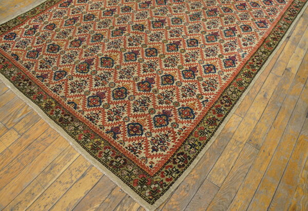 Beige rug with repeating orange, blue, and green geometric medallions rests on distressed wooden floorboards.