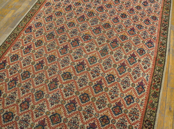 Traditional beige rug with an all-over geometric red and navy pattern, bordered in green, lying on wood planks.