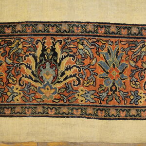 Cream rug field meets a wide orange border displaying detailed blue and yellow traditional floral motifs.
