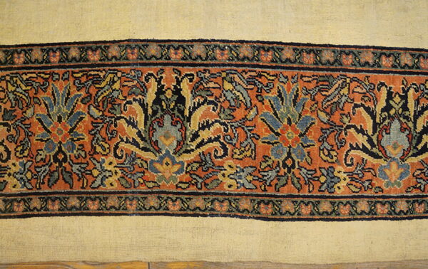 Cream rug field meets a wide orange border displaying detailed blue and yellow traditional floral motifs.