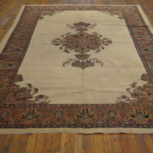 Beige traditional rug featuring a large central medallion and intricate coral borders rests on wood plank flooring.