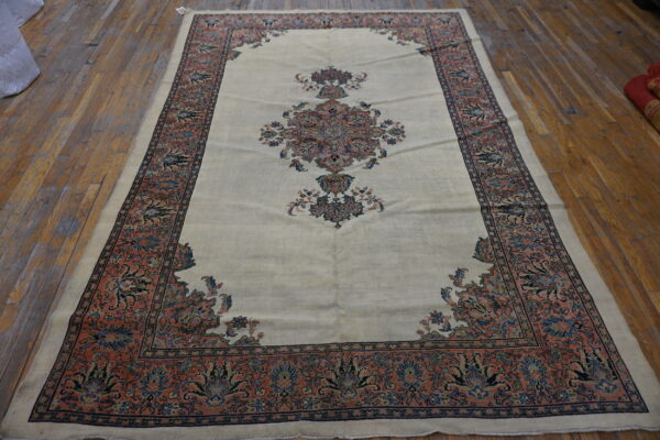 Low-pile cream rug with intricate blue and coral traditional patterns on distressed wood planks.