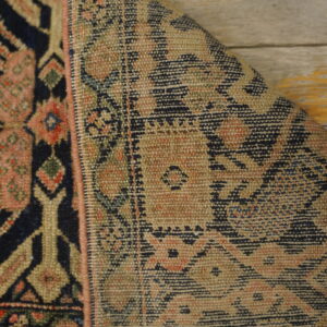 Folded rug corner displays navy and pink geometric patterns next to the lighter, flat woven reverse side on wood flooring.