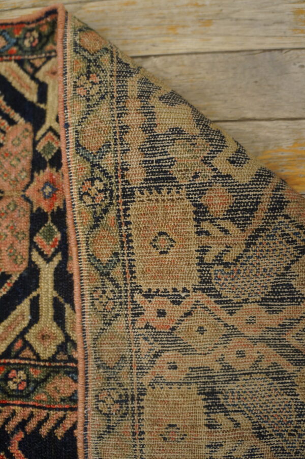 Folded rug corner displays navy and pink geometric patterns next to the lighter, flat woven reverse side on wood flooring.