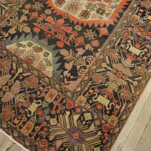 Ornate dark rug with stylized red, gold, and pink patterns lying on light wood plank flooring.