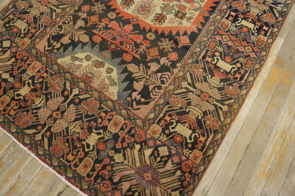 Ornate dark rug with stylized red, gold, and pink patterns lying on light wood plank flooring.
