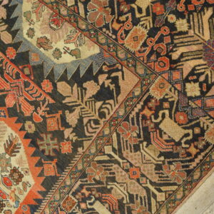 Detailed view of a dark tribal rug with complex red, tan, and blue patterns on whitewashed wooden planks.