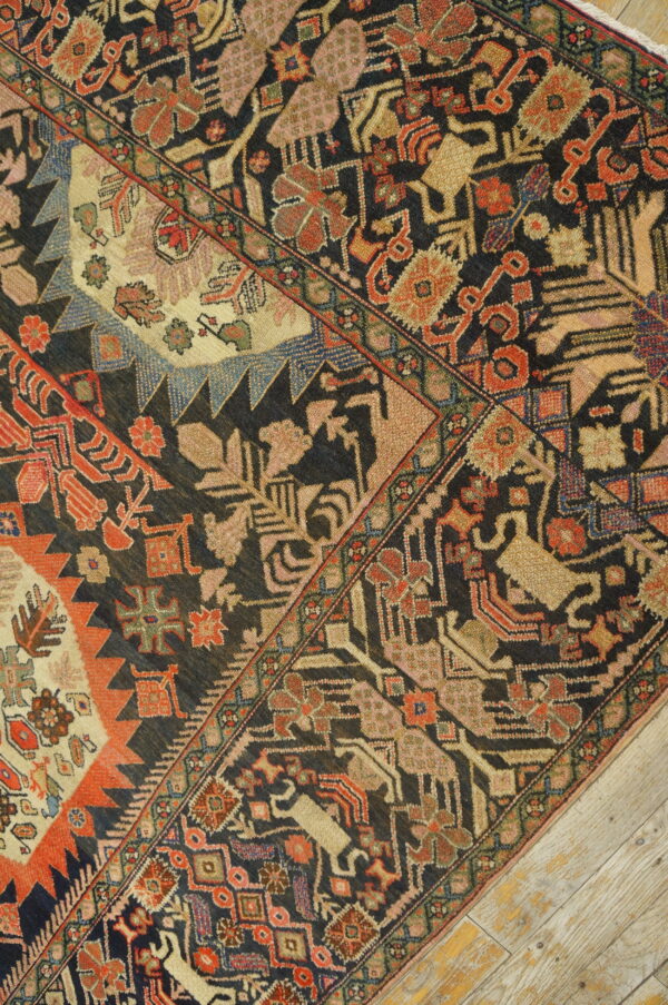 Detailed view of a dark tribal rug with complex red, tan, and blue patterns on whitewashed wooden planks.