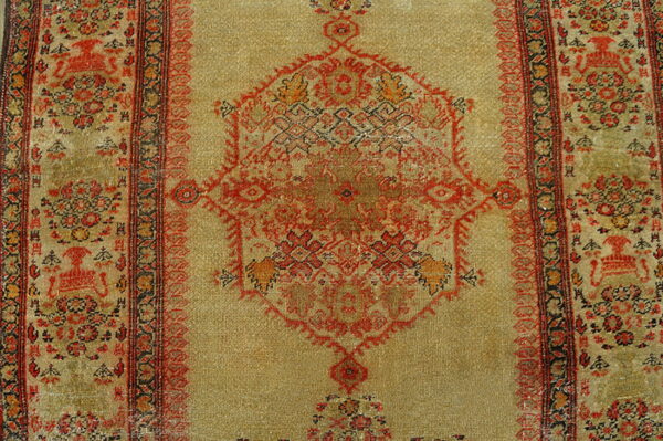Low-pile rug with a pale gold field, red geometric medallion, and detailed, dark ornamental borders.