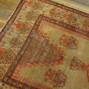 Close up of a distressed gold and rust patterned rug with low pile on weathered wooden floorboards.