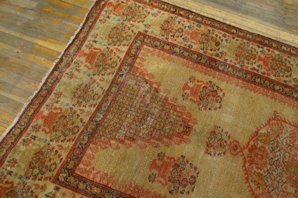 Close up of a distressed gold and rust patterned rug with low pile on weathered wooden floorboards.