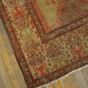 Distressed khaki and red patterned rug with fringe resting on worn yellow wood planks.